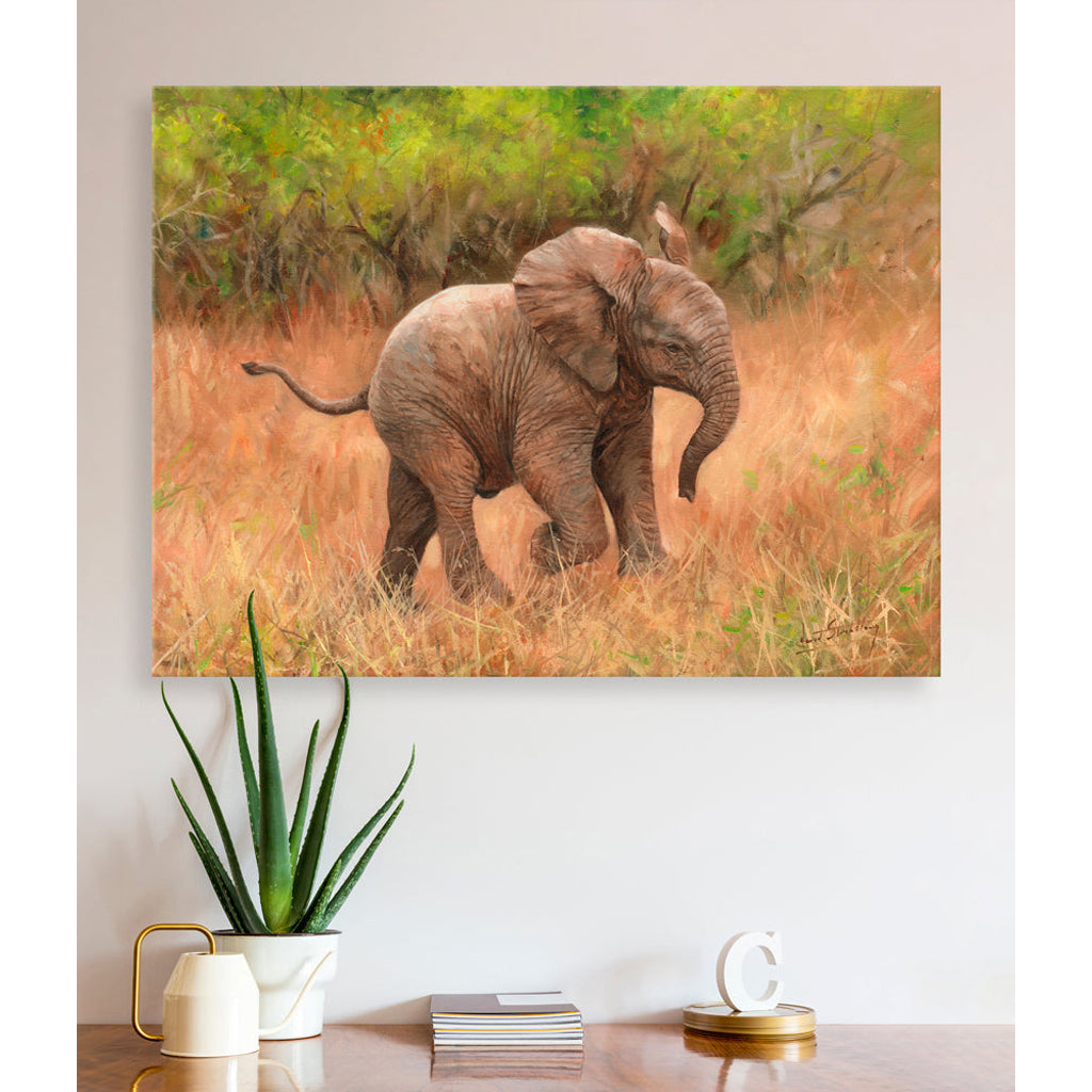 Canvas print of an elephant calf in a natural setting on a wall above a desk with decor items.