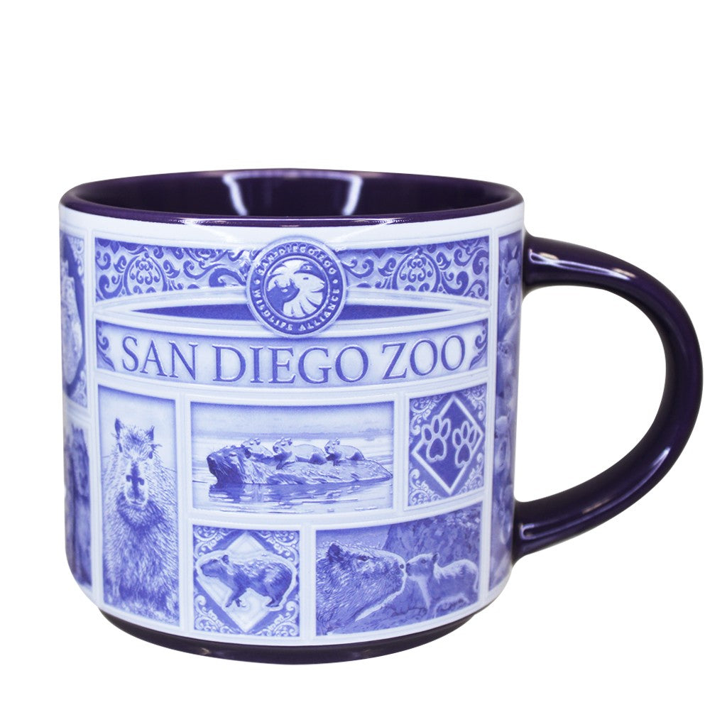 A ceramic San Diego Zoo & Safari Park mug with a white exterior decorated in blue with the San Diego Zoo logo, capybara portraits, and scenic illustrations, featuring a dark blue handle and interior.