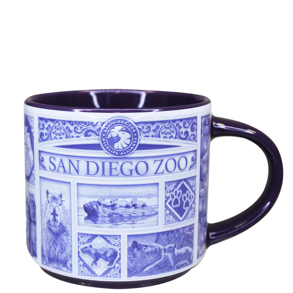 A ceramic San Diego Zoo & Safari Park mug with a white exterior decorated in blue with the San Diego Zoo logo, capybara portraits, and scenic illustrations, featuring a dark blue handle and interior.