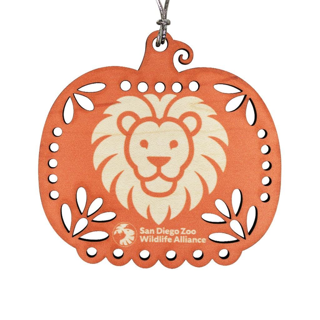 An orange laser-cut wooden pumpkin ornament featuring a cream-colored lion face in the center and the San Diego Zoo Wildlife Alliance logo at the bottom, hanging from a silver string against a white background.