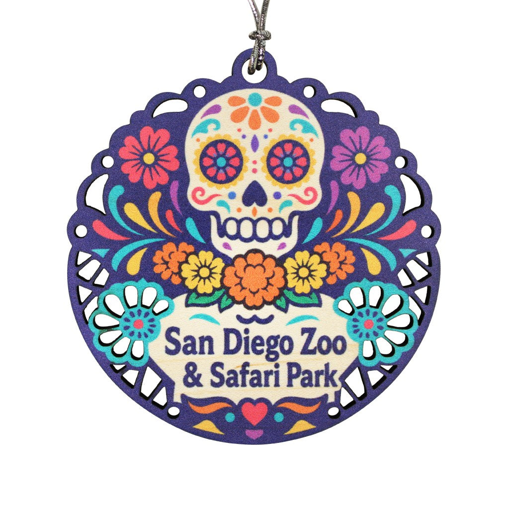A round decorative hanging wooden ornament with a colorful sugar skull and floral Day of the Dead style design. The center reads 'San Diego Zoo &amp; Safari Park' and the ornament hangs from a silver cord.