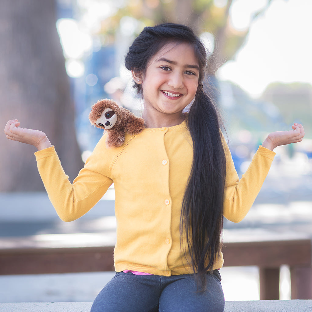 A young girl in a yellow sweater holding a Sloth Shoulder Friends Mini Plush toy outdoors.