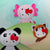Hello Kitty wildlife plushies- a giant panda, an axolotl, and a red panda with bows on a light green background.