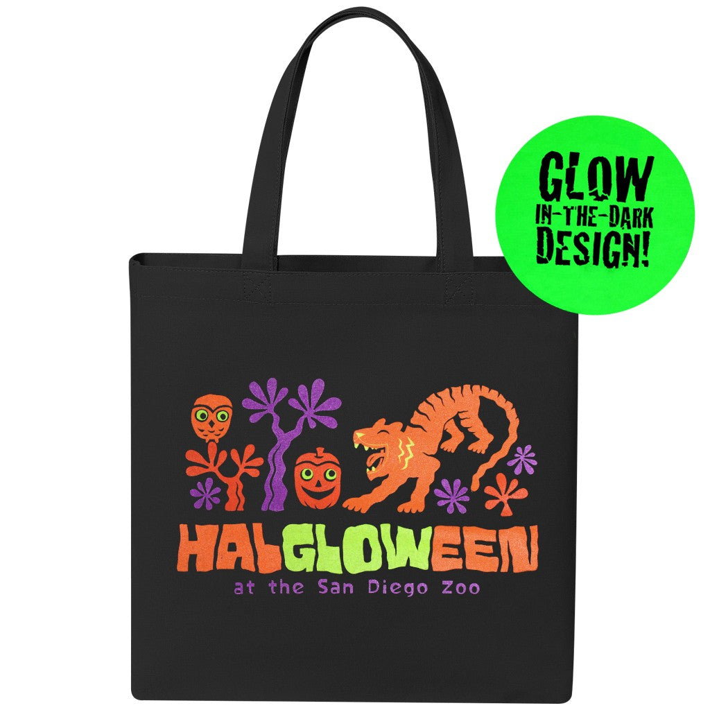 A black canvas tote bag with a colorful Halloween-themed graphic reading 'HALLOWEEN at the San Diego Zoo' in neon-style lettering. The design includes orange pumpkins, a tiger, purple flowers, and a green circular badge that says 'GLOW IN THE DARK DESIGN!'.