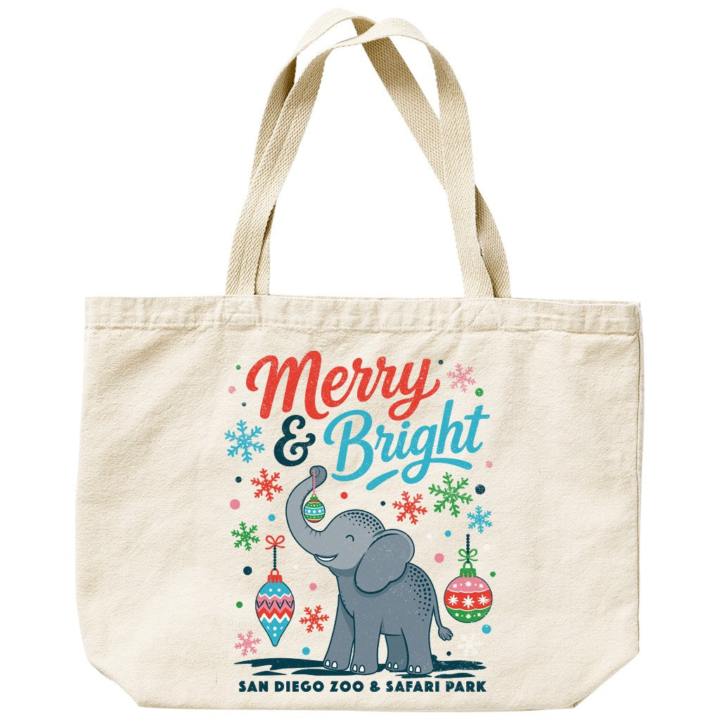 A natural canvas tote bag with a festive Christmas graphic featuring a gray elephant, colorful ornaments, snowflakes, and the text 'Merry & Bright' and 'SAN DIEGO ZOO & SAFARI PARK'.